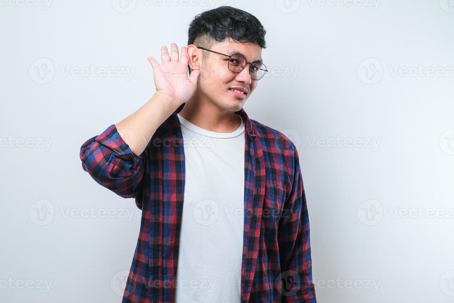 Junger gutaussehender asiatischer Mann, der mit der Hand über dem Ohr lächelt und Gerüchten oder Klatsch zuhört. Taubheitskonzept. foto