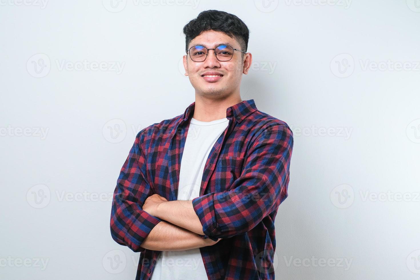 Porträt eines jungen gutaussehenden asiatischen Mannes mit lässigem Hemd und Brille, der mit verschränkten Armen steht und in die Kamera lächelt foto