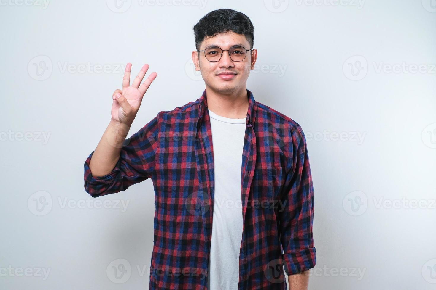 junger gutaussehender asiatischer mann, der lässige kleidung trägt und mit den fingern nummer drei nach oben zeigt, während er selbstbewusst und glücklich lächelt foto