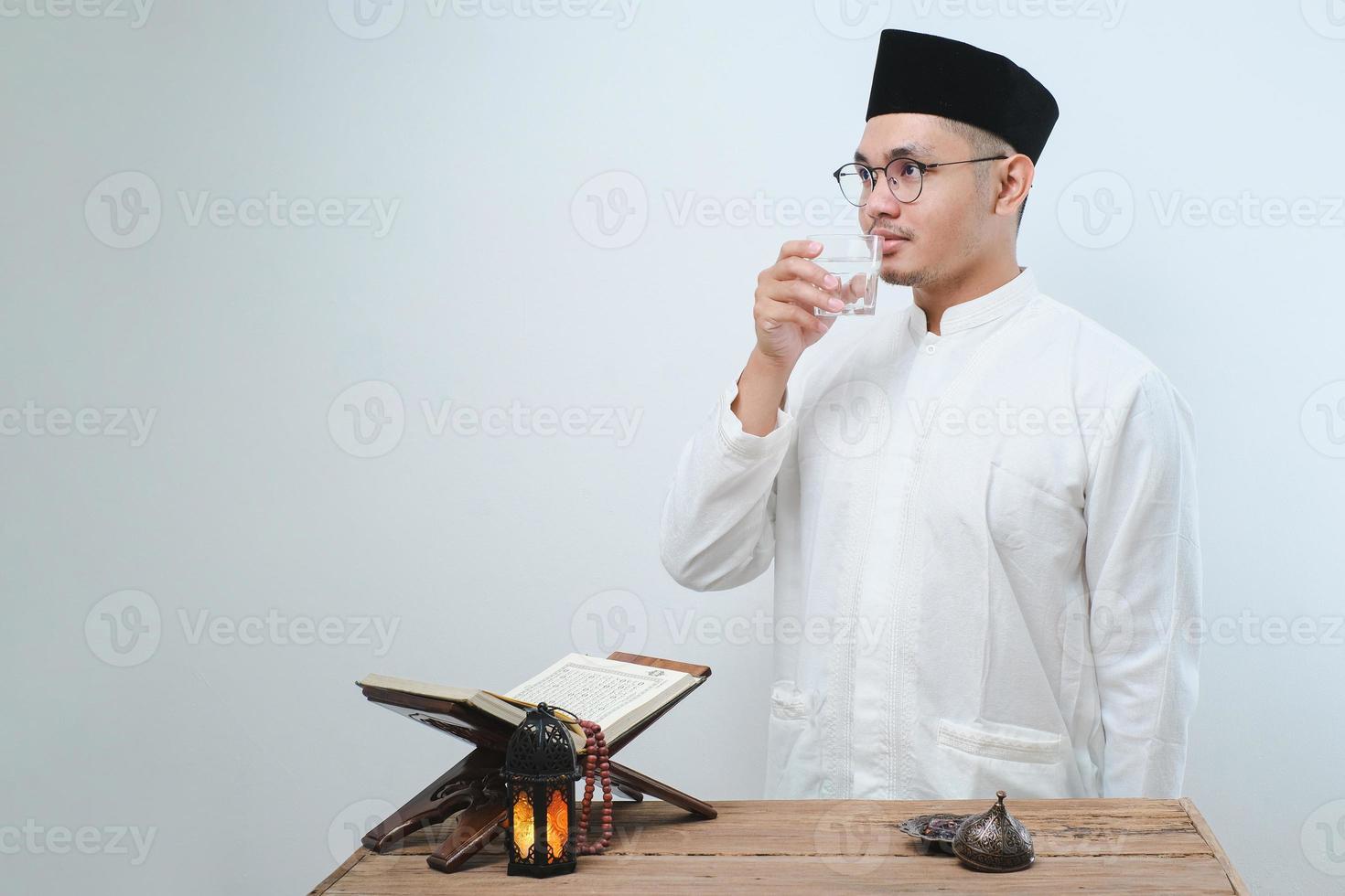 asiatischer muslimischer Mann lächelt und Daumen hoch, während er ein Glas Wasser zum Fastenbrechen trinkt foto