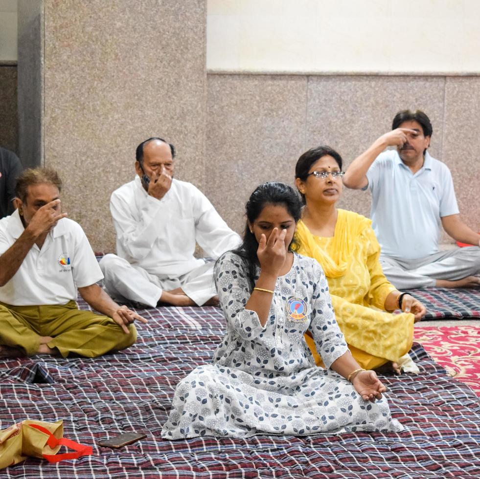 neu-delhi, indien, 19. juni 2022 - gruppen-yoga-übungssitzung für menschen verschiedener altersgruppen im balaji-tempel, vivek vihar, internationaler yoga-tag, große gruppe von erwachsenen, die an yoga-kursen im tempel teilnehmen foto