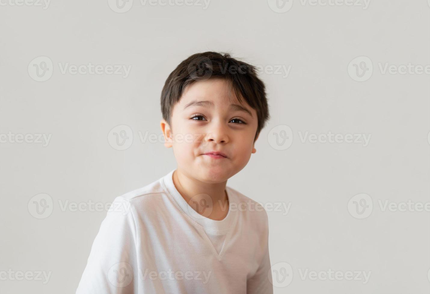 Porträt süßer glücklicher kleiner Junge mit weißem T-Shirt, der mit überraschtem Gesicht aufschaut, positives Kind mit lächelndem Gesicht in den Kopf geschossen und lustiges Gesicht macht. Konzept der Kindertage foto