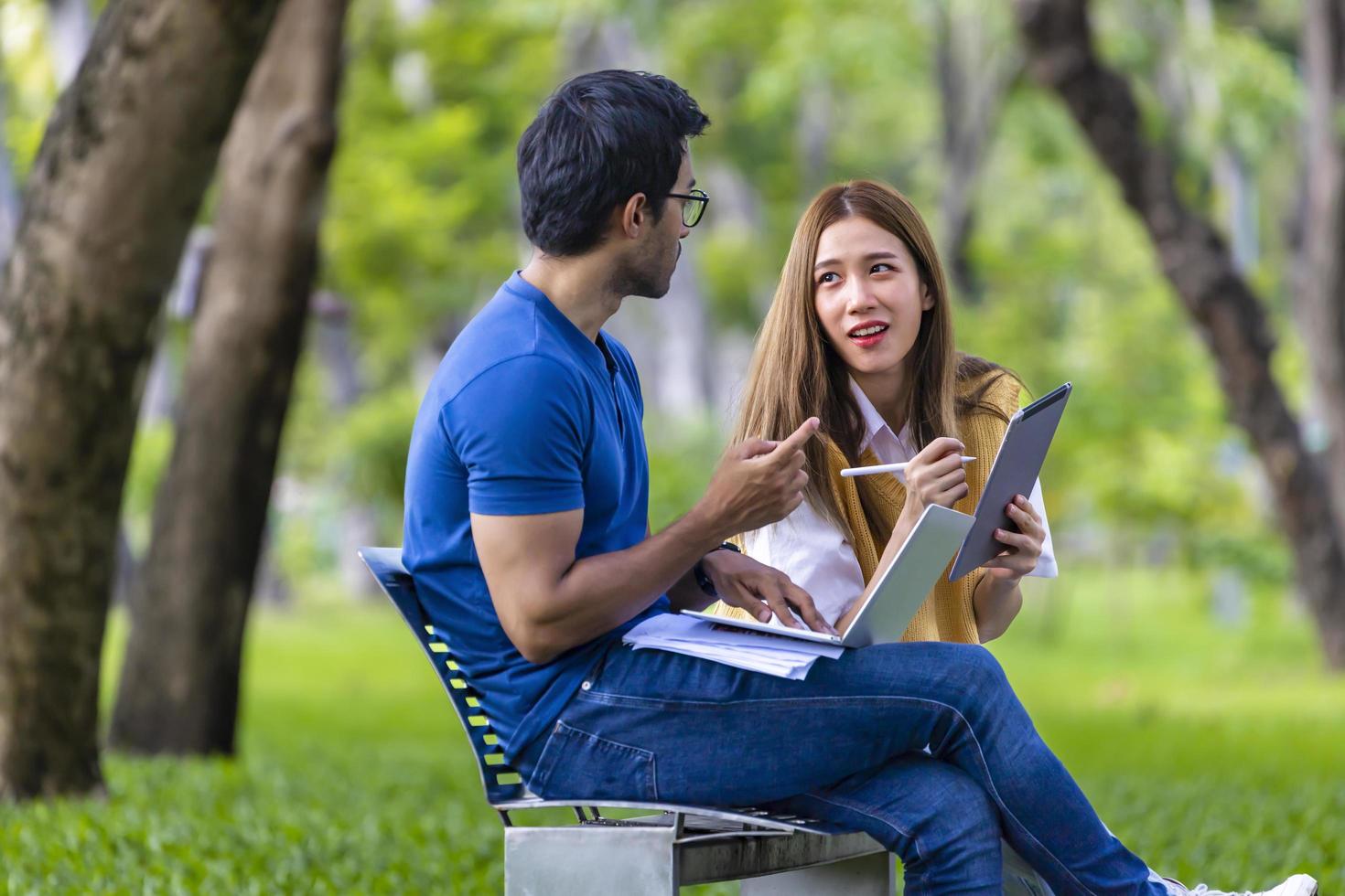 junge asiatische und indische studenten verbringen gerne eine entspannte zeit auf dem universitätscampus, während sie am wochenende zusammen auf der bank sitzen und lernen foto