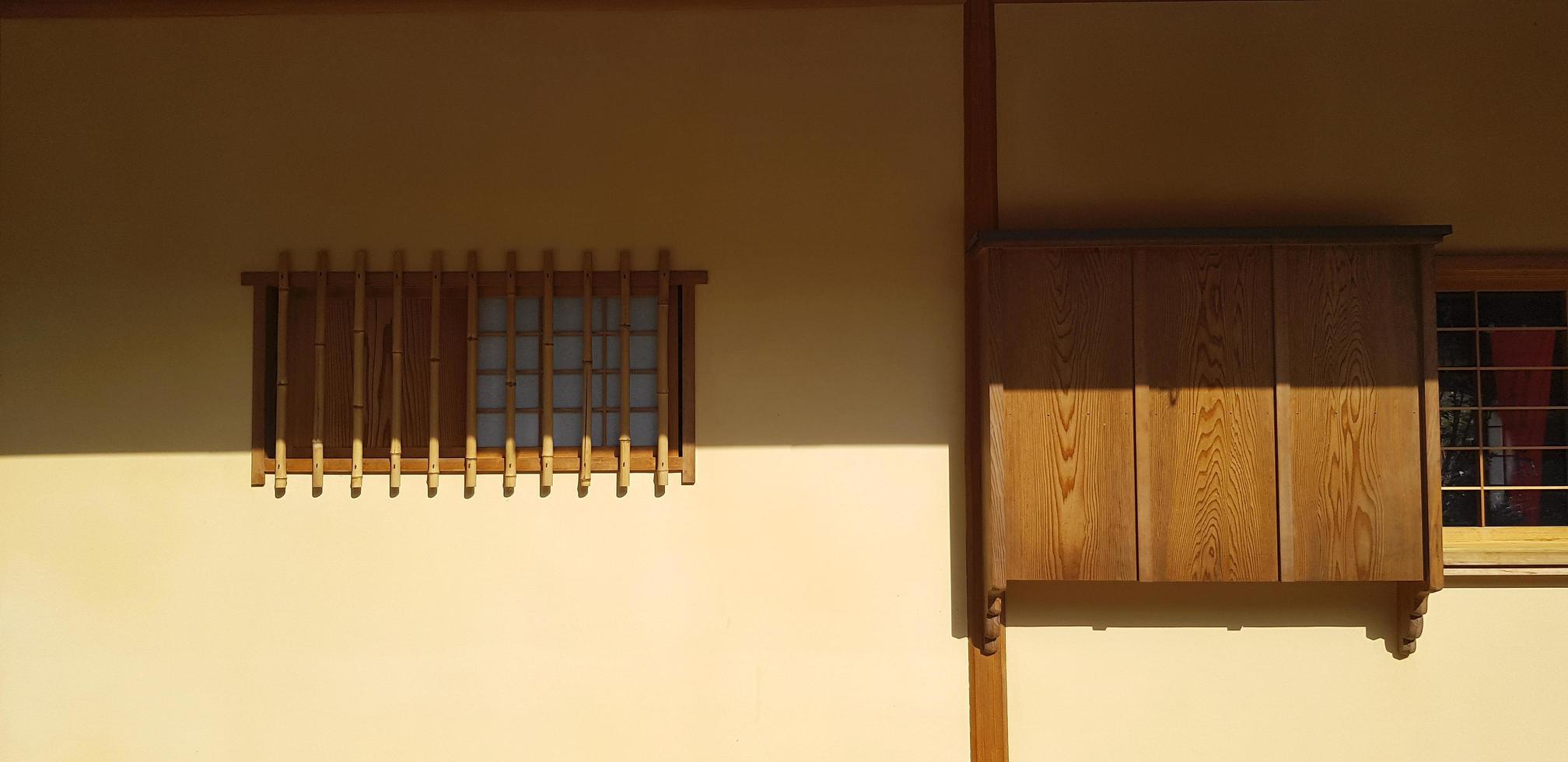 braunes holz- und trockenes bambusfenster mit schatten auf gelbem betonwandhintergrund in. außengestaltung durch verwendung von natürlichem material zum bau von häusern oder häusern in japan. Objekt dekoriert und Kunst des Lichts. foto