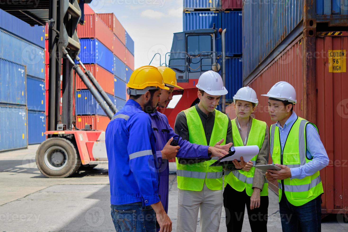 Eine Gruppe gemischtrassiger Arbeiter in Sicherheitsuniformen und Hardhats arbeitet am Logistikterminal mit vielen Containerstapeln und verlädt Kontrollversandgüter für die Frachttransportindustrie. foto