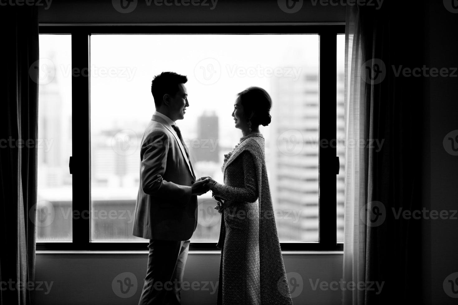 Der Bräutigam steht und hält während der Verlobungszeremonie die Hand am Hochzeitskleid an die Braut. schwarz-weiß-foto nach der tradition von thailand, die braut trägt traditionelle thailändische kleidung. foto