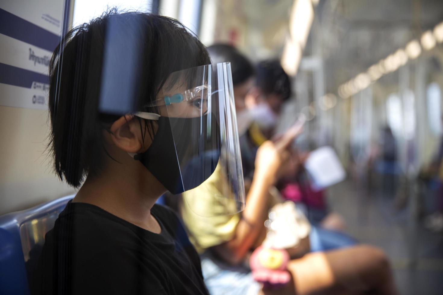 junge asiatin, die eine chirurgische gesichtsmaske trägt, die vor der ausbreitung des krankheitsvirus covid-19 oder der ausbruchsprävention des coronavirus sitzt, sitzt in der u-bahn im öffentlichen bereich foto