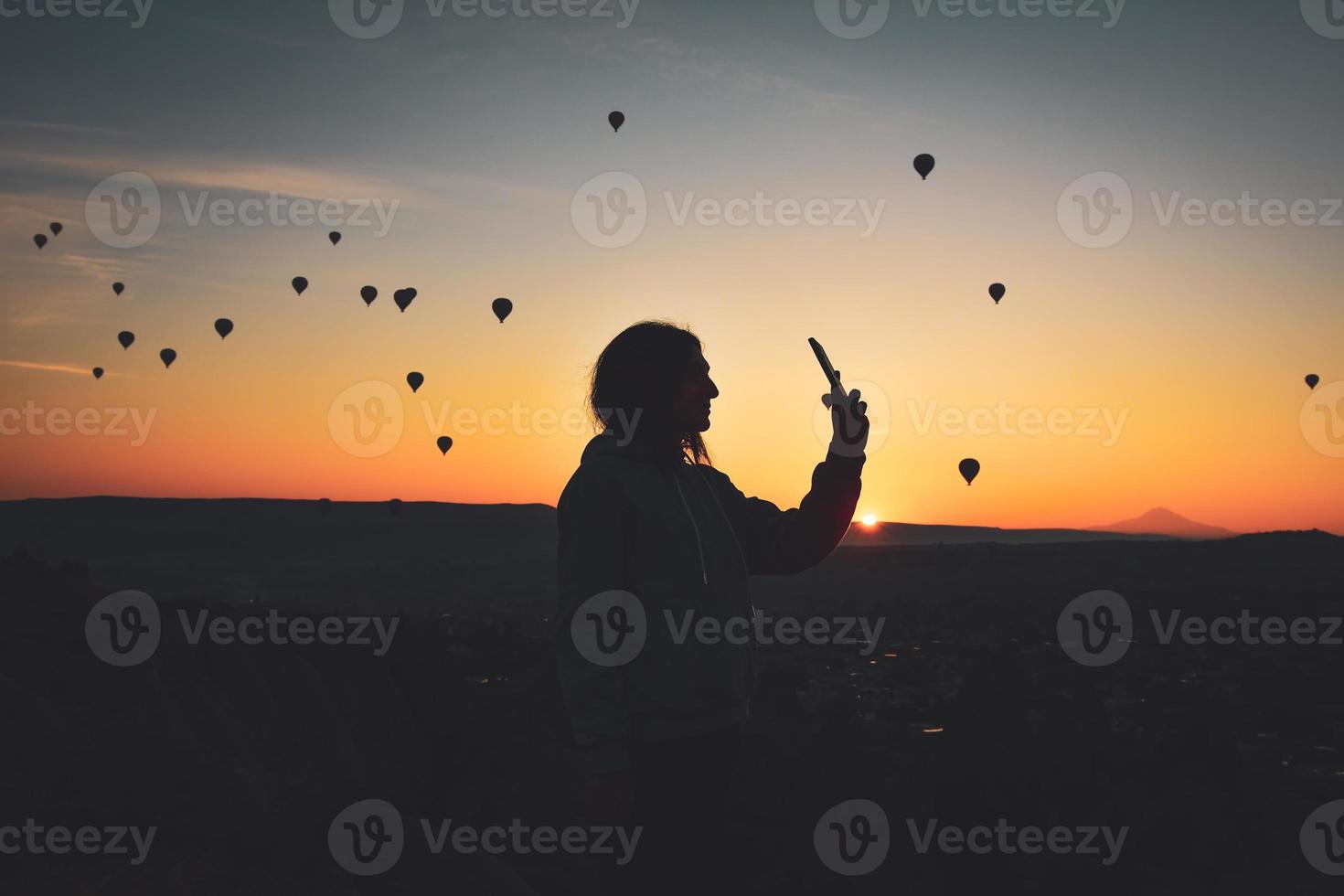 silhouette des smartphones in den händen einer frau, die fotos einer wunderschönen landschaft und luftballons in kappadokien macht. Sonnenaufgangszeit, verträumtes Reisekonzept