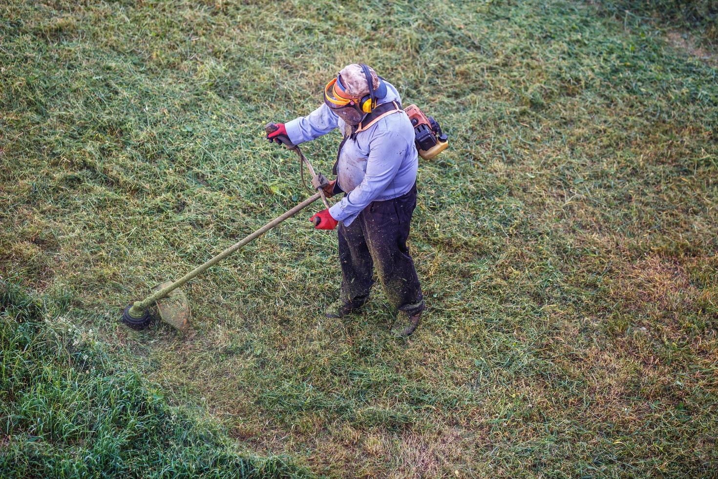 draufsicht fetter schmutziger rasenmäher mann arbeiter schneiden trockenes gras mit rasenmäher. foto