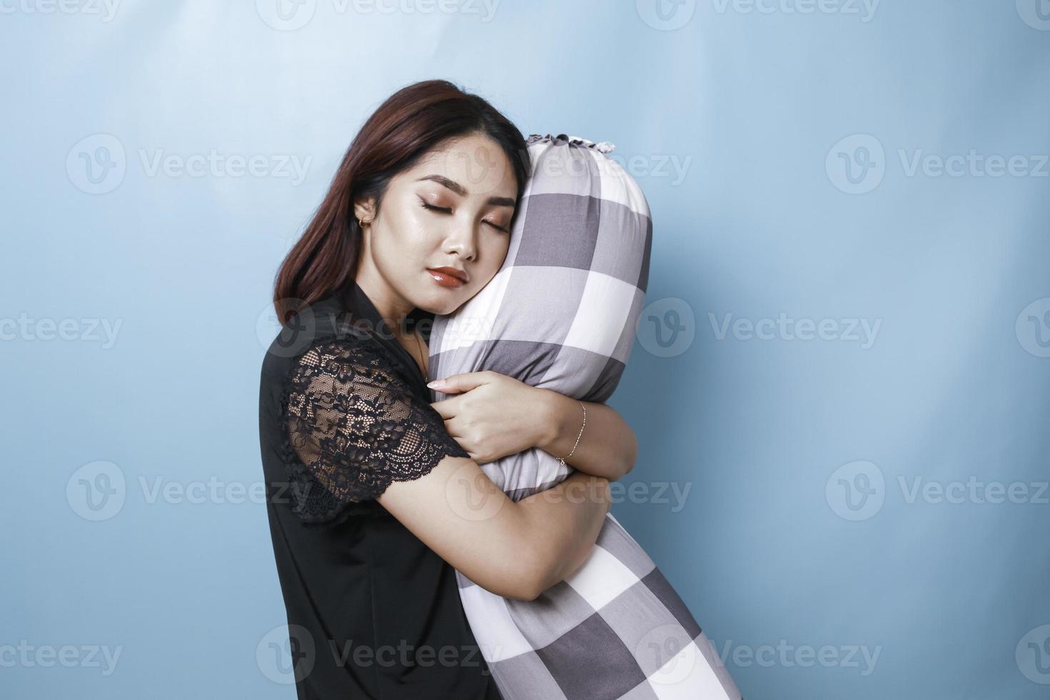 porträt einer verschlafenen, attraktiven asiatischen frau, die einen pyjama trägt und ein polster beim einschlafen hält foto