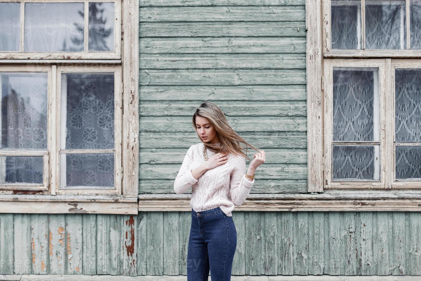 hübsche Frau in einem Strickpullover auf dem Hintergrund eines alten Holzhauses mit Fenstern foto