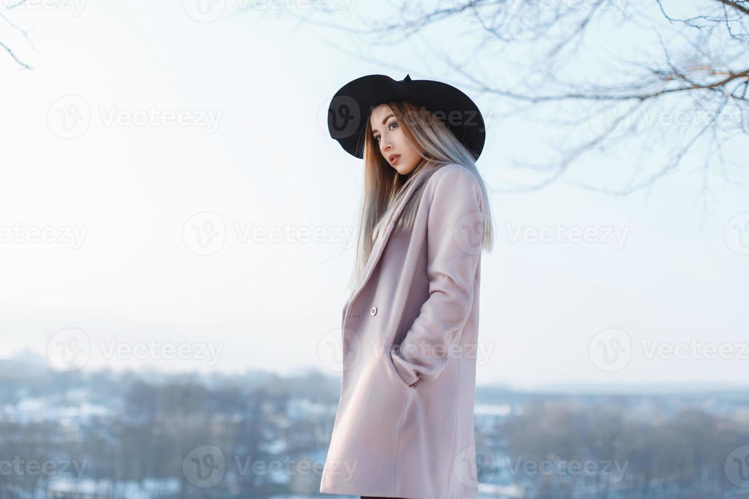 junges schönes Mädchen in schwarzem Hut und Mantel auf dem Hintergrund einer Winterlandschaft foto