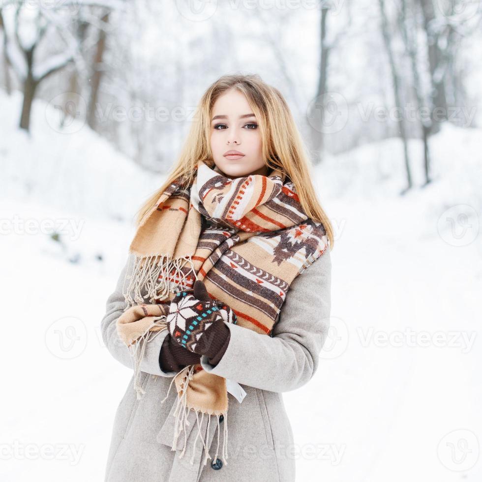 Schöne Frau mit Vintage-Strickschal, die in einem Winterpark in der Nähe eines Baumes steht. foto