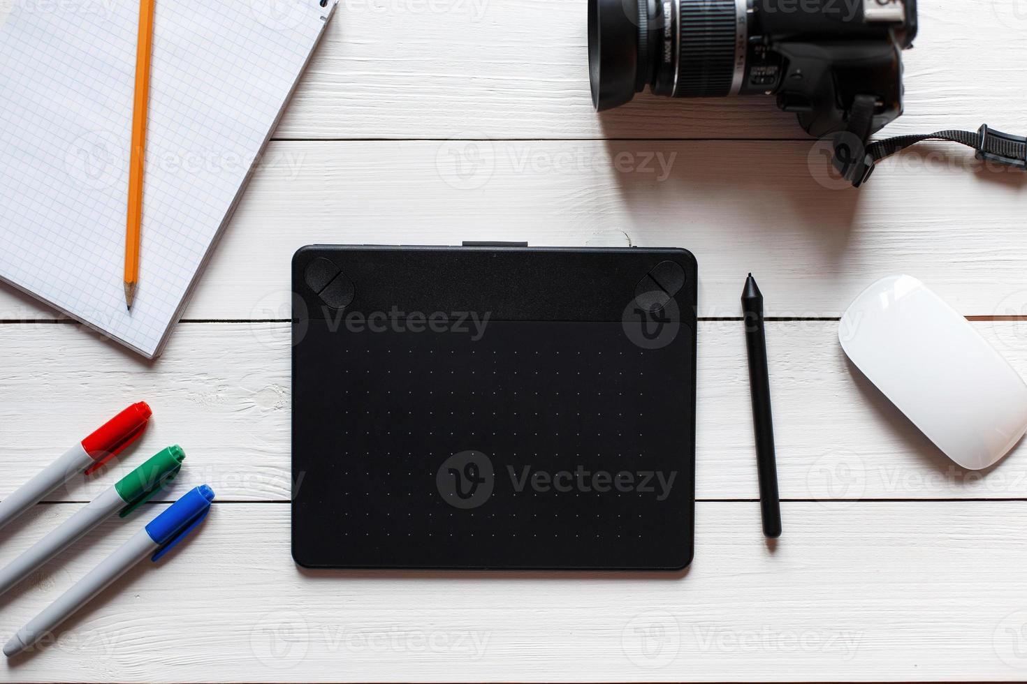 Konzeptkünstler-Desktop. Grafiktablett, Kamera, Notizbuch mit Bleistift und Markierungen auf einem weißen Holztisch. Sicht von oben foto