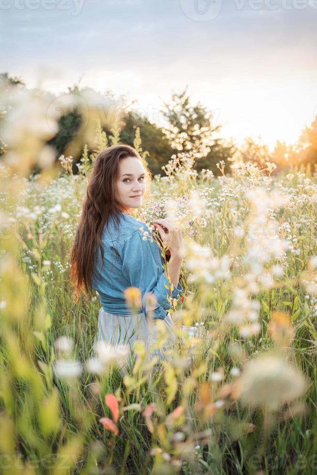 schönes Mädchen, das im Sommer mit Wildblumen auf dem Feld spazieren geht. foto