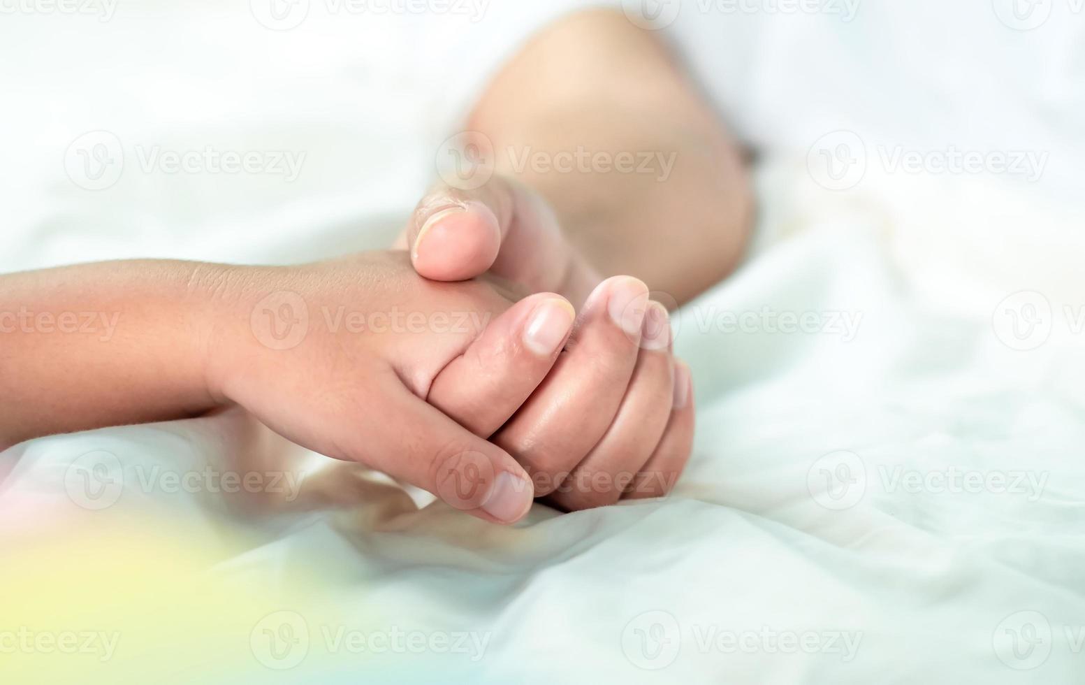 nahaufnahme mutter, die die hand des babys auf weißem bett hält, liebe bindung, ermutigung und wärme kümmern sich in der familie umeinander, familienkonzept foto