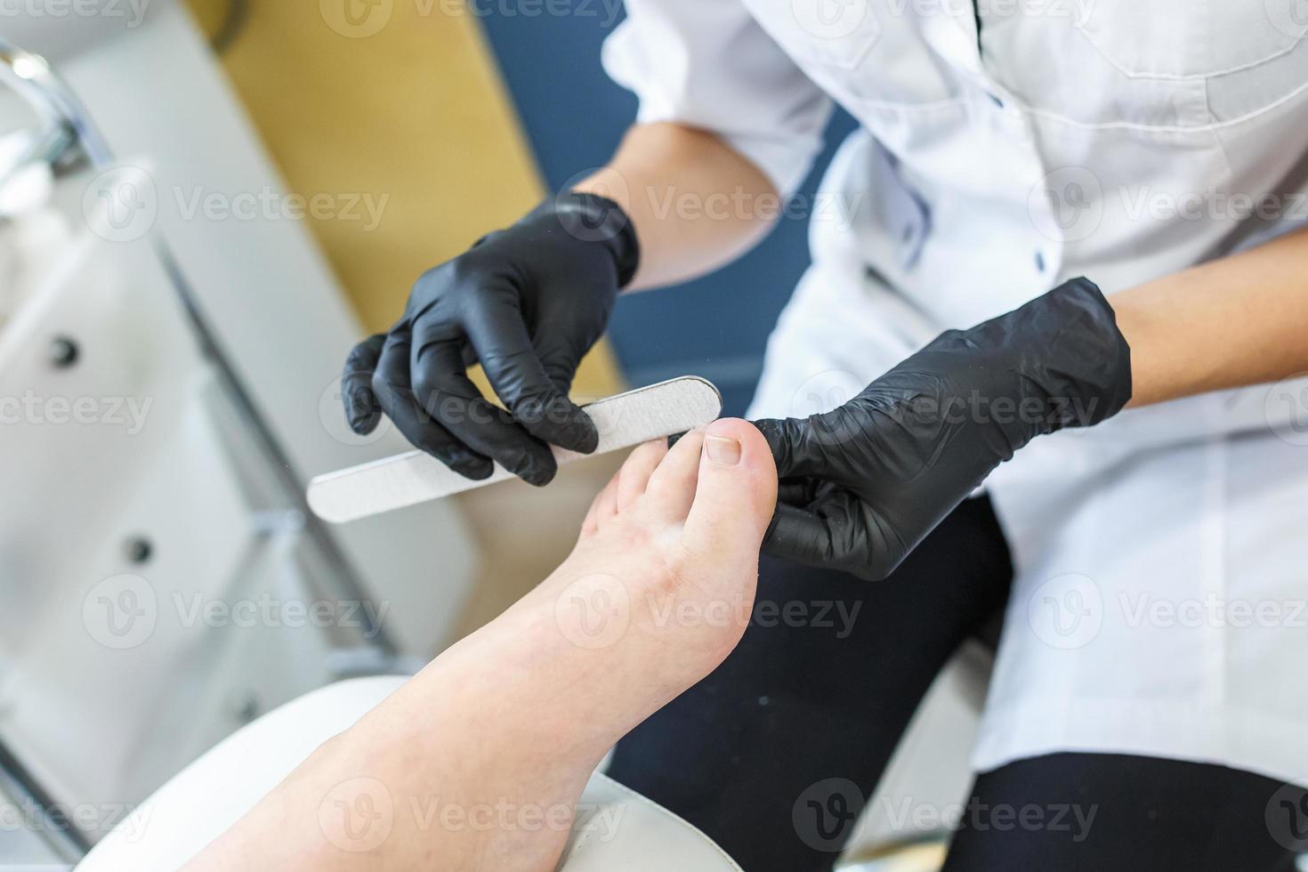 der Meister in schwarzen Handschuhen im Salon macht Maniküre-Pediküre für den Kunden foto