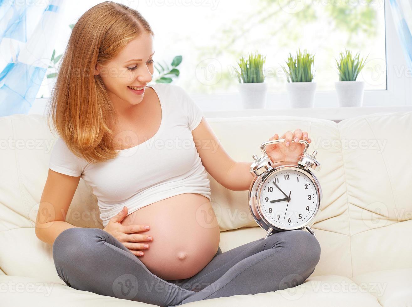 Schwangerschaftskonzept. glückliche schwangere Frau mit einem Wecker foto