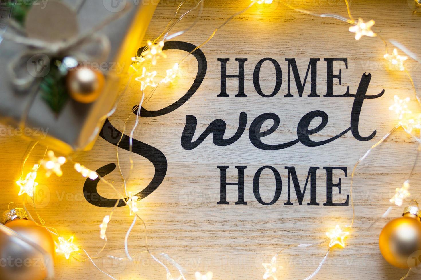 Home Sweet Home - die Inschrift auf der Tafel im Weihnachtsdekor, Lichterketten, eine Schachtel mit einem Geschenk für das neue Jahr. Hintergrund foto
