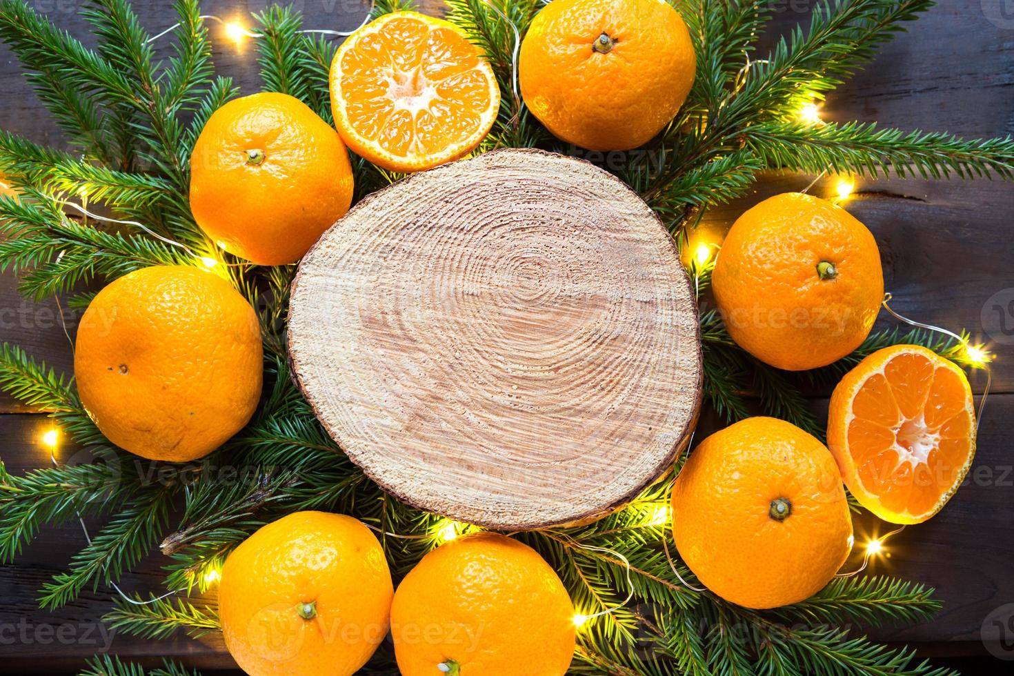 neujahrsfeiertagshintergrund auf rundem baumschnitt, umgeben von mandarinen, lebenden tannenzweigen und goldenen lichtergirlanden, mit holzplatz für text. Zitrusaroma, Orangenscheiben, Weihnachten. rahmen foto