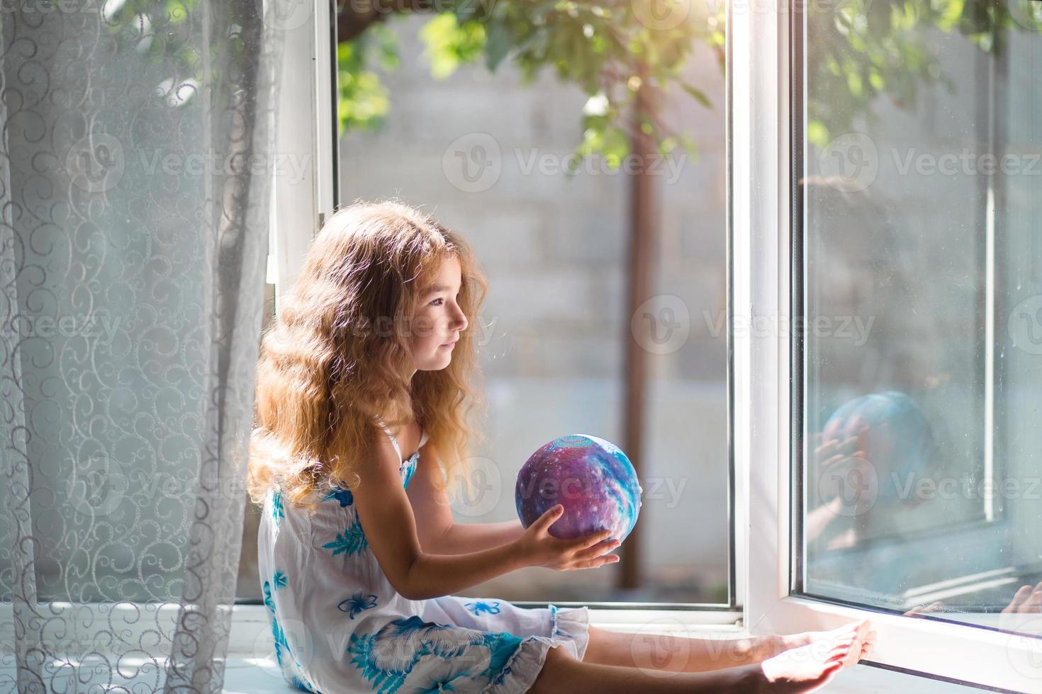 Das Mädchen am Fenster des Hauses hält eine Lampe in Form eines Planeten, einer Kugel. Frieden, Ökologie, Umwelt, friedlich foto