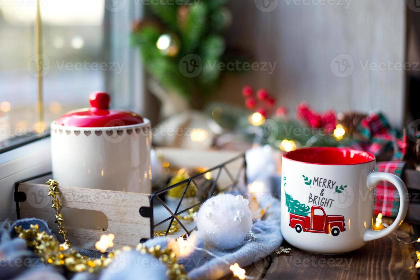 Weihnachtsdekoration am Fenster auf einer gemütlichen Holzfensterbank mit einem Becher mit einem Getränk und einer Keksdose. Lichterketten, Weihnachtsbaumzweig, Frühstückstablett-Stillleben foto