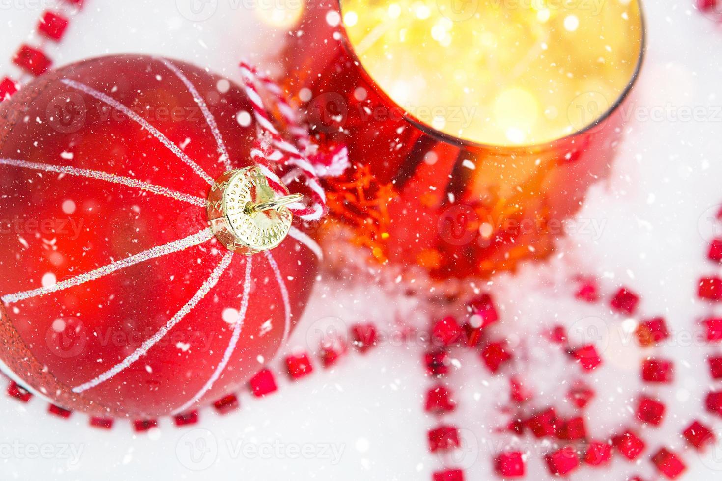 roter Weihnachtsball auf natürlichem weißem Schnee mit quadratischen Perlen und brennender Kerze in einem Glaskerzenhalter. weihnachten, neujahr im freien. Schneefall, festliche Stimmung von Märchen und Magie, Straßendekoration. foto