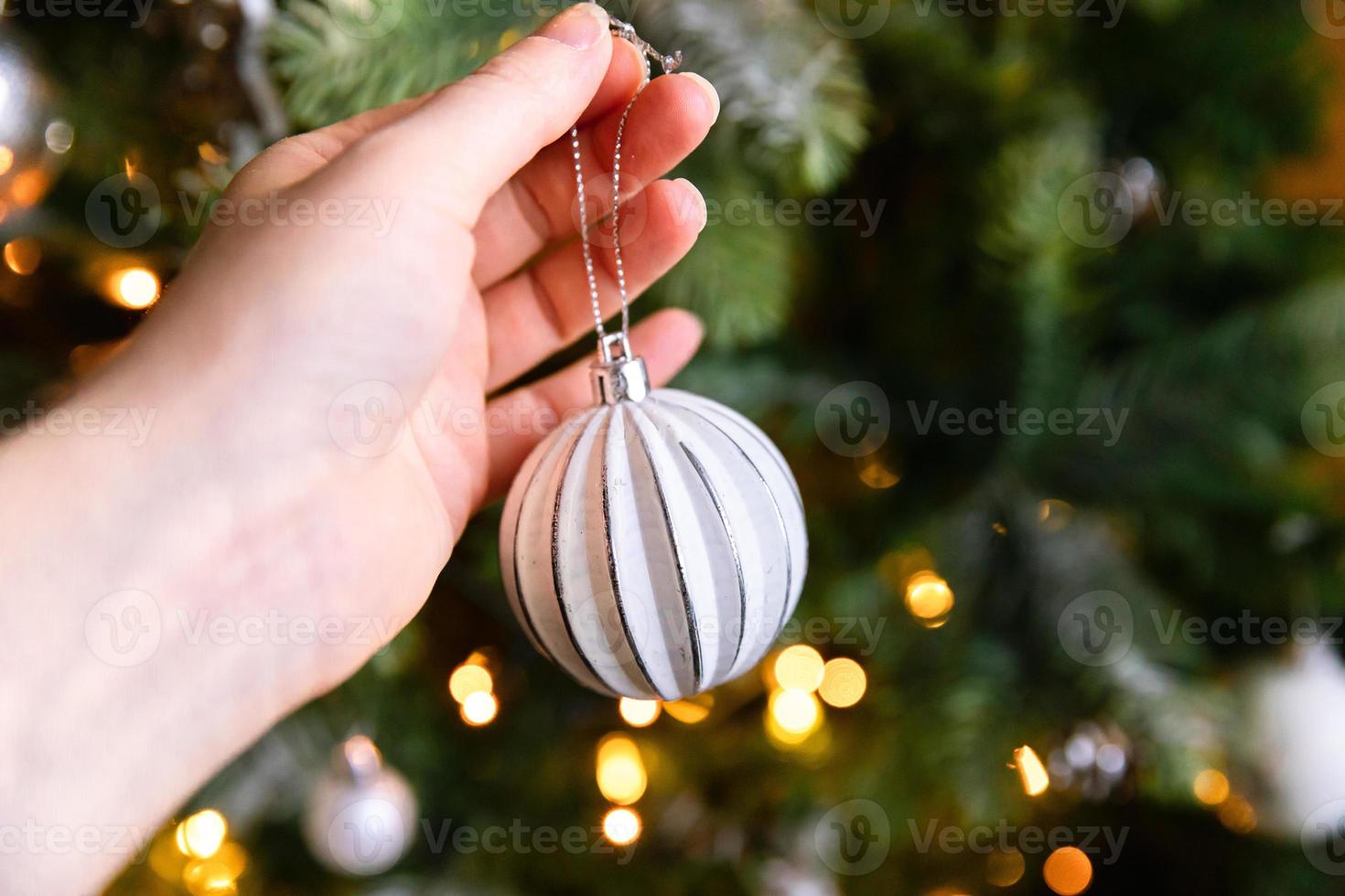 Frauenhand, die Weihnachtsbaum schmückt. weihnachtsbaum mit weißen und silbernen dekorationen, ornamenten spielzeug und ball. moderne Innenarchitektur im klassischen Stil. Heiligabend zu Hause, Zeit zum Feiern. foto