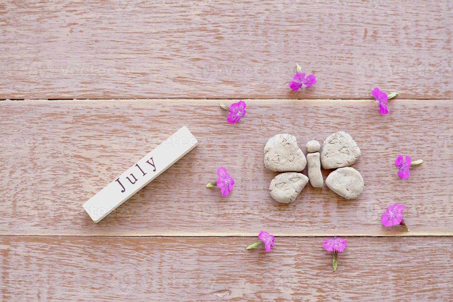 Draufsicht des Holzkalenders mit Julizeichen, Tonschmetterling und rosa Blumen. foto