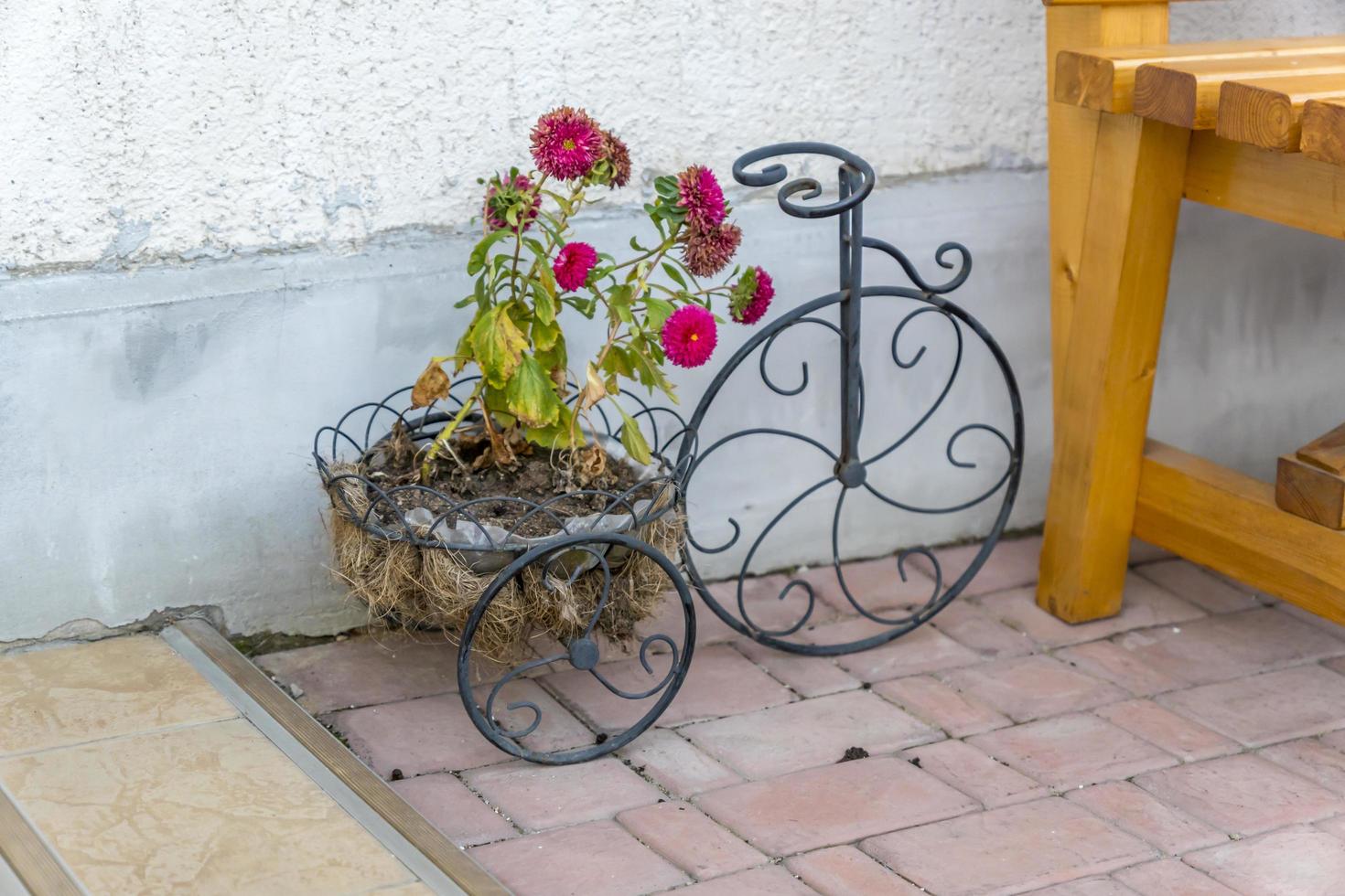 dekoratives fahrrad mit blumenbeet an der wand in der nähe der bank foto