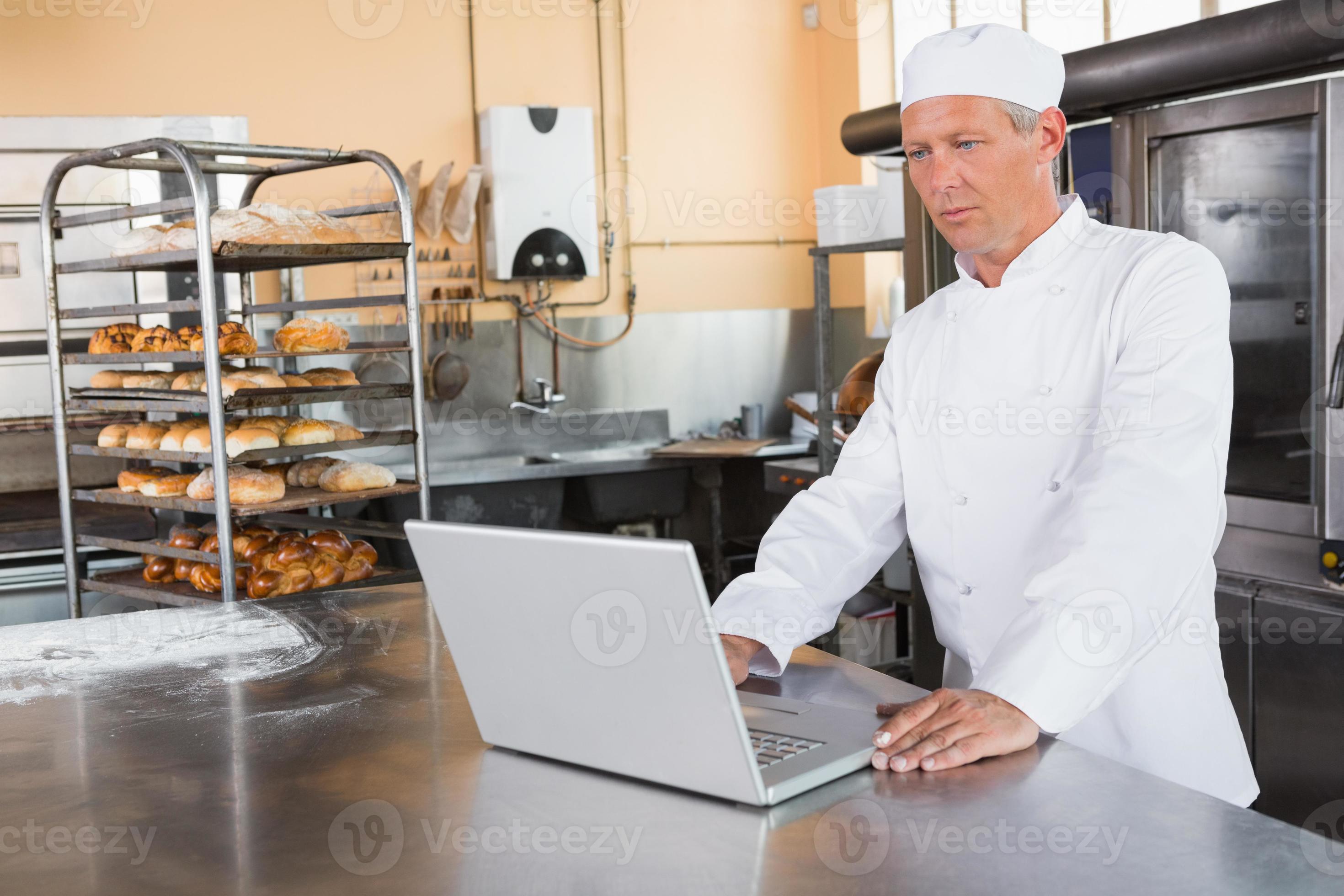 fokussierter Bäcker mit Laptop auf Arbeitsplatte foto