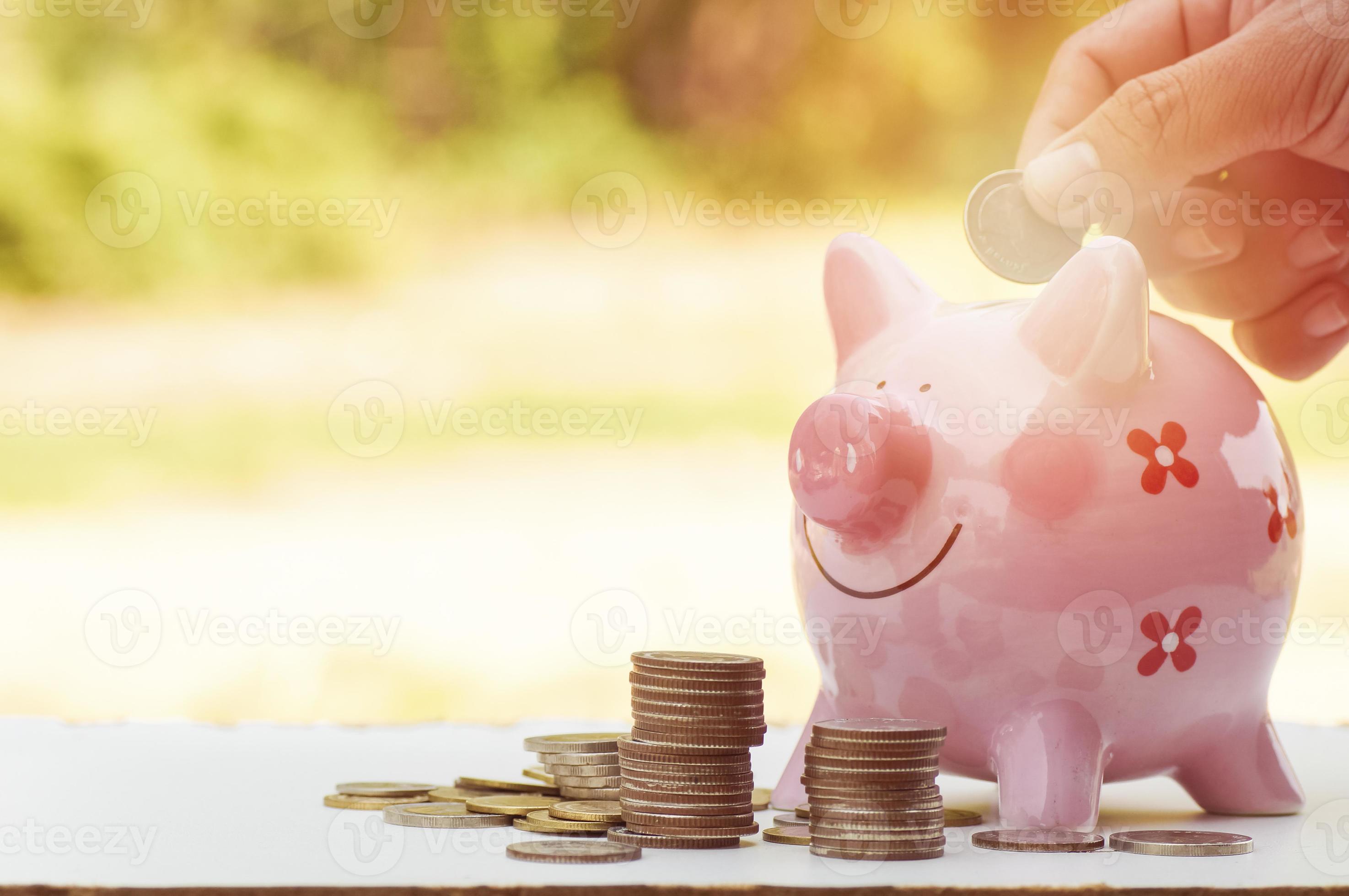 Hand, die Geld in ein rosa Sparschwein legt foto