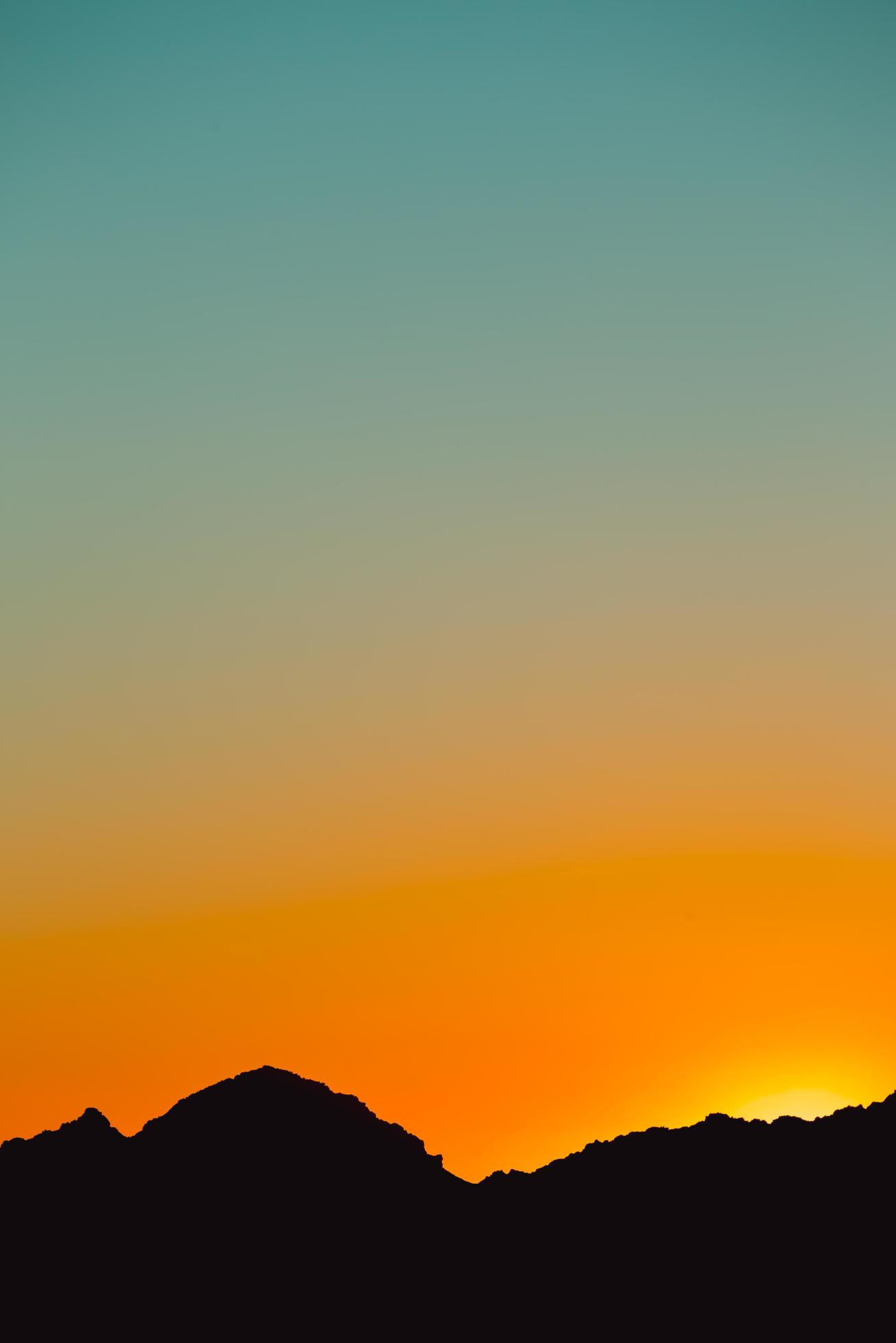 eine Silhouette eines Berges in Schwarz mit einem Gradienten des Sonnenuntergangshimmels in Orange und Blau foto