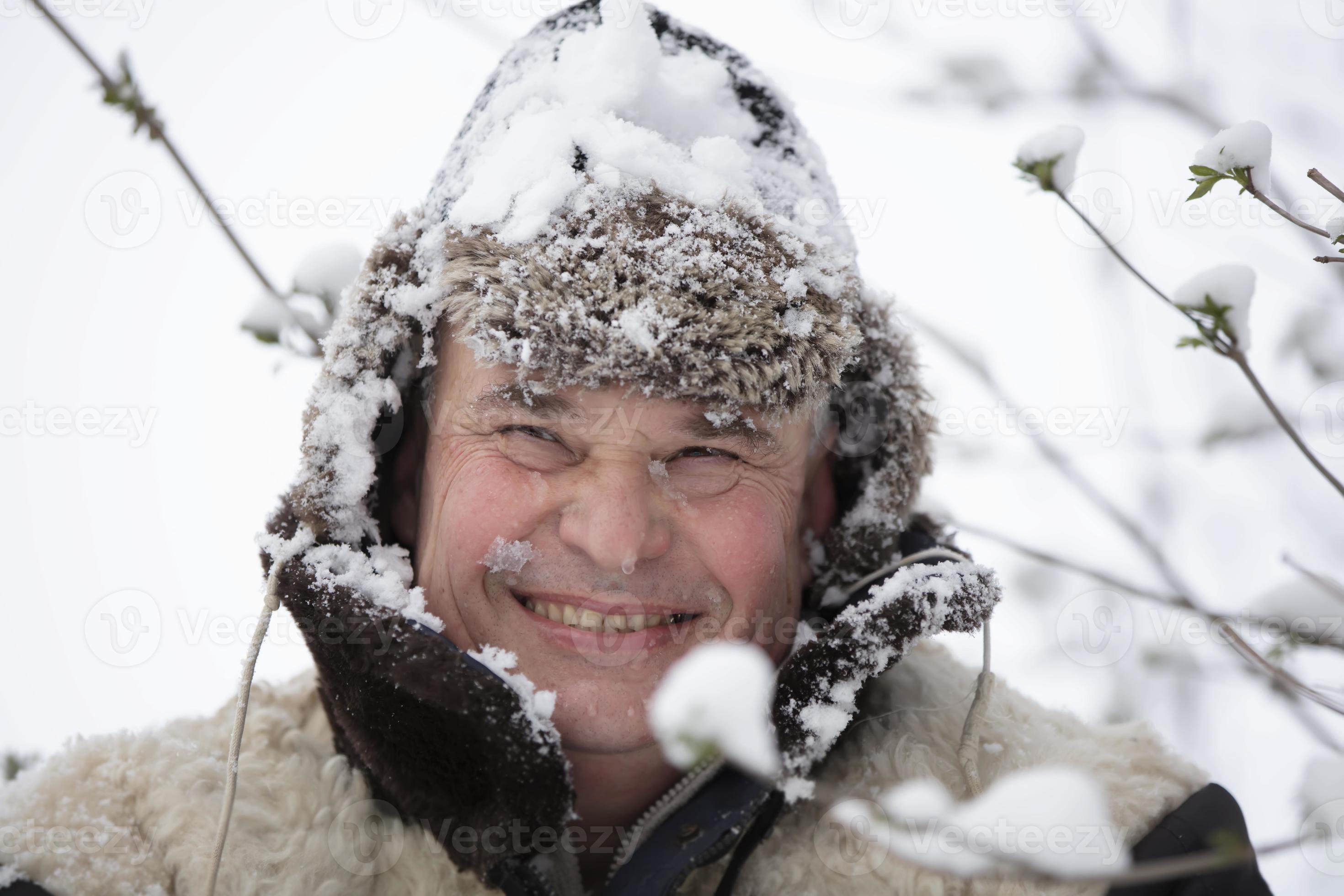ein Alten Mann im ein Winter Hut bedeckt mit Schnee lächelt und