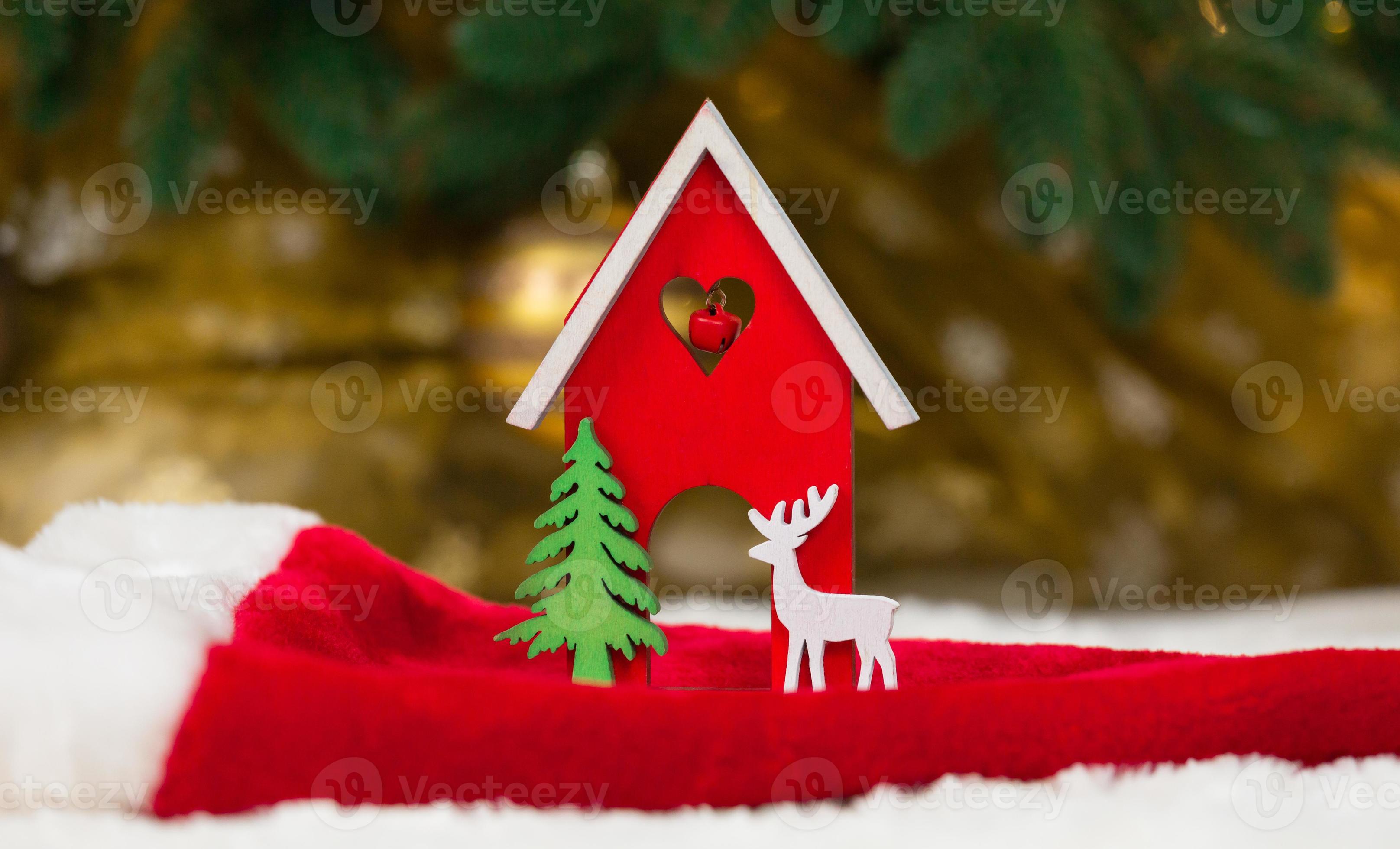 hölzernes hölzernes Spielzeughaushirsch und -baum auf einer Weihnachtsmütze und einer weißen Decke, die Schnee imitiert foto