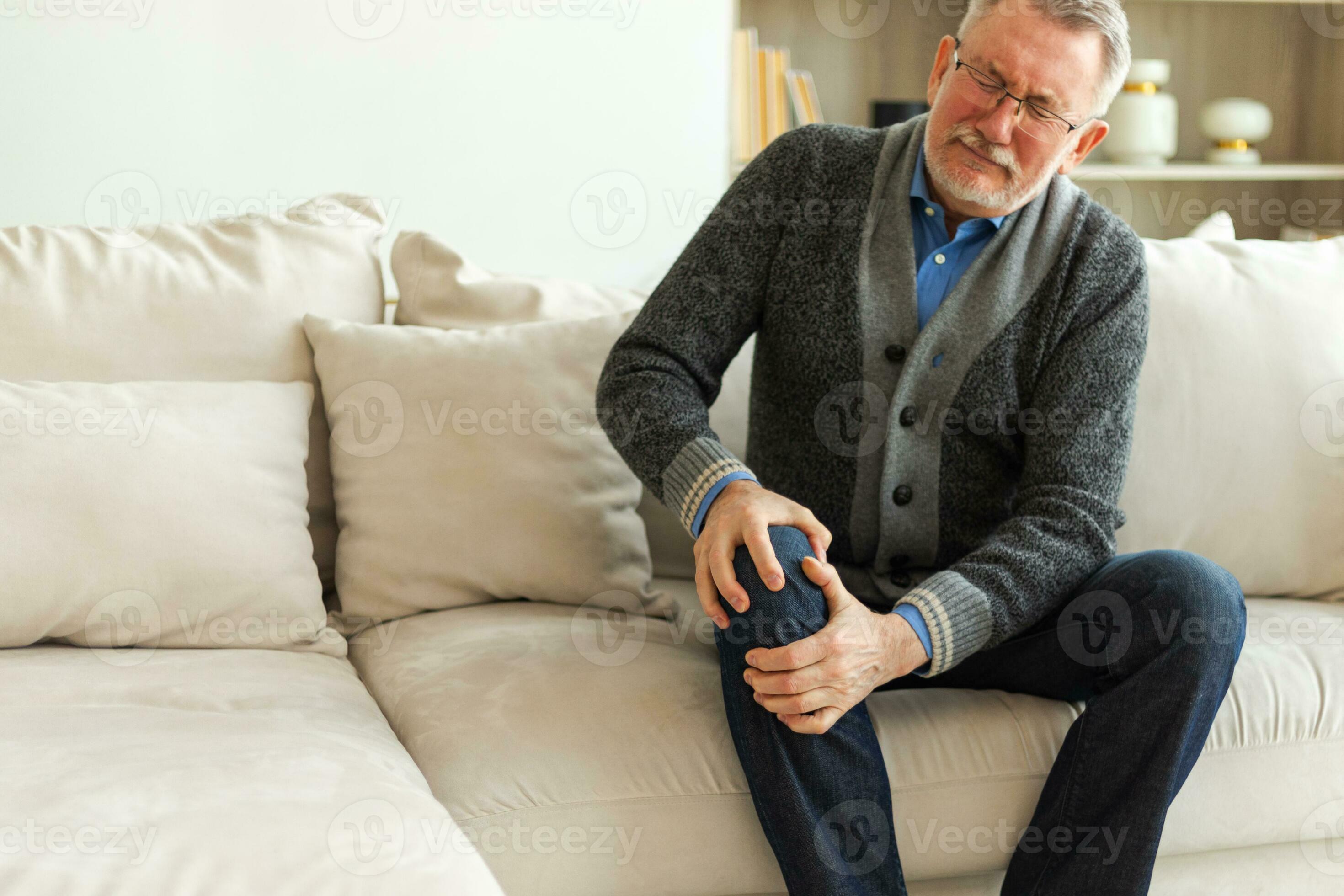 Knie Schmerzen Arthritis Körper krank Gesundheit Pflege Konzept.  unzufrieden Mitte alt Senior Mann Leiden von Knie schmerzen Sitzung auf  Sofa beim heim, reifen alt Senior Großvater berühren Bein Gefühl Schmerzen  verletzt im
