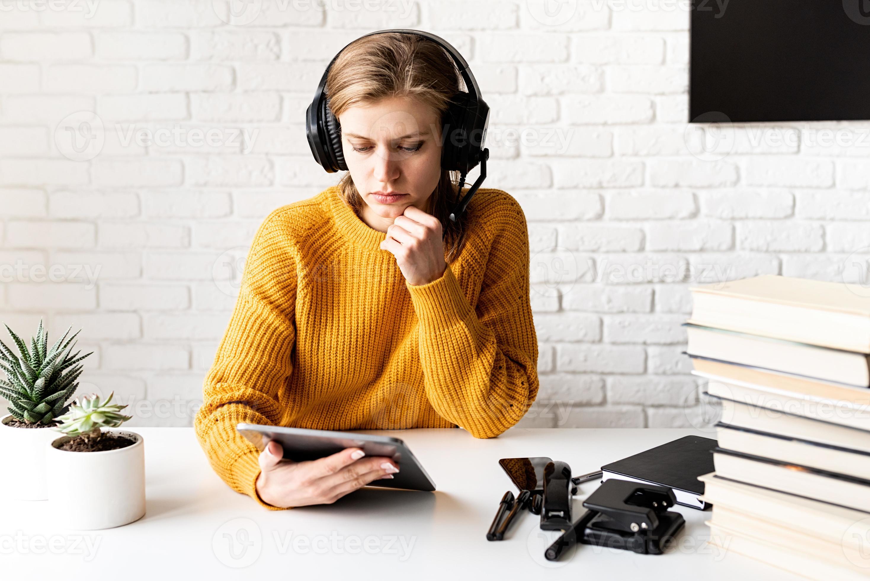 Frau in schwarzen Kopfhörern, die online mit digitalem Tablet studiert foto