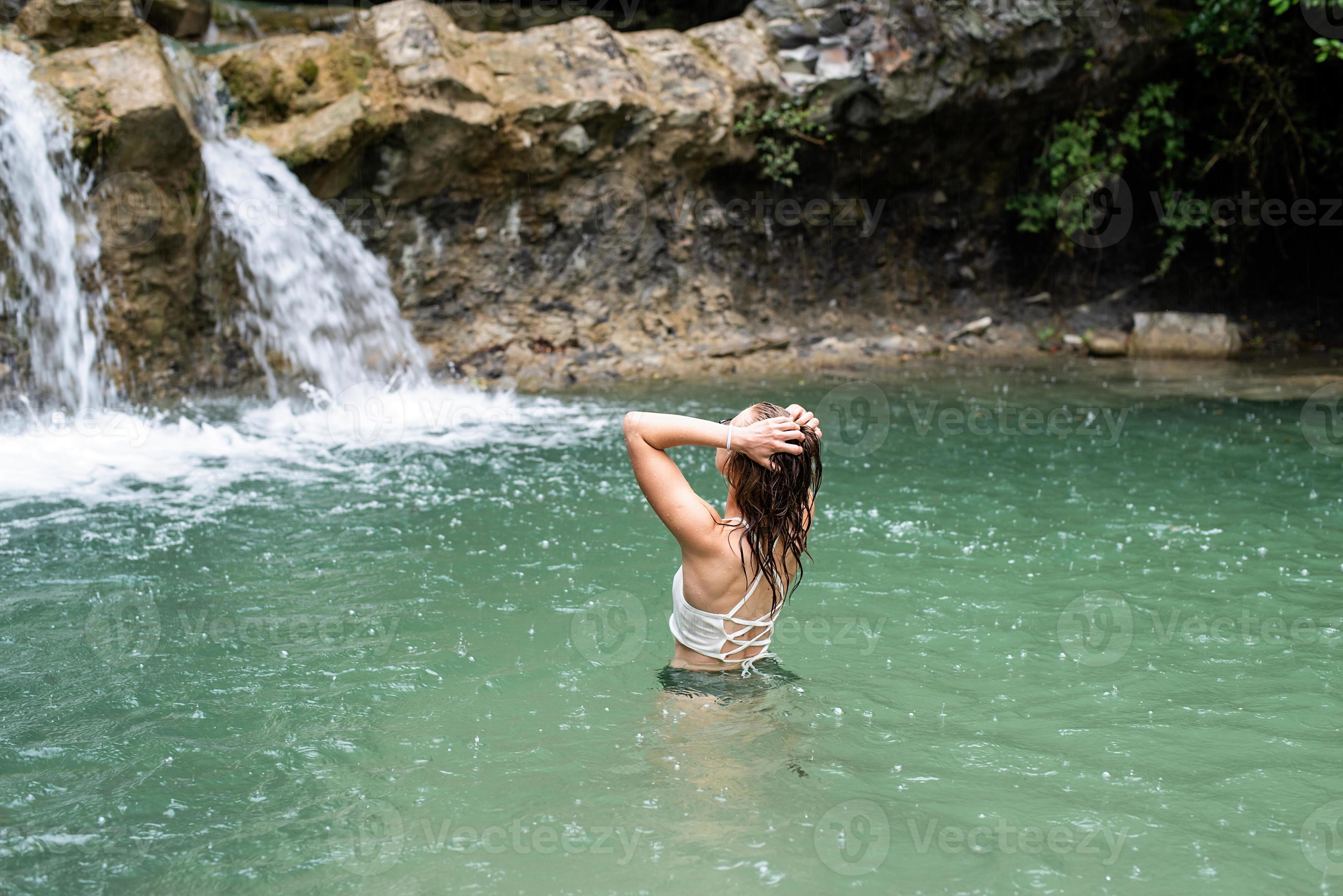 Frau schwimmt im Bergfluss mit Wasserfall foto
