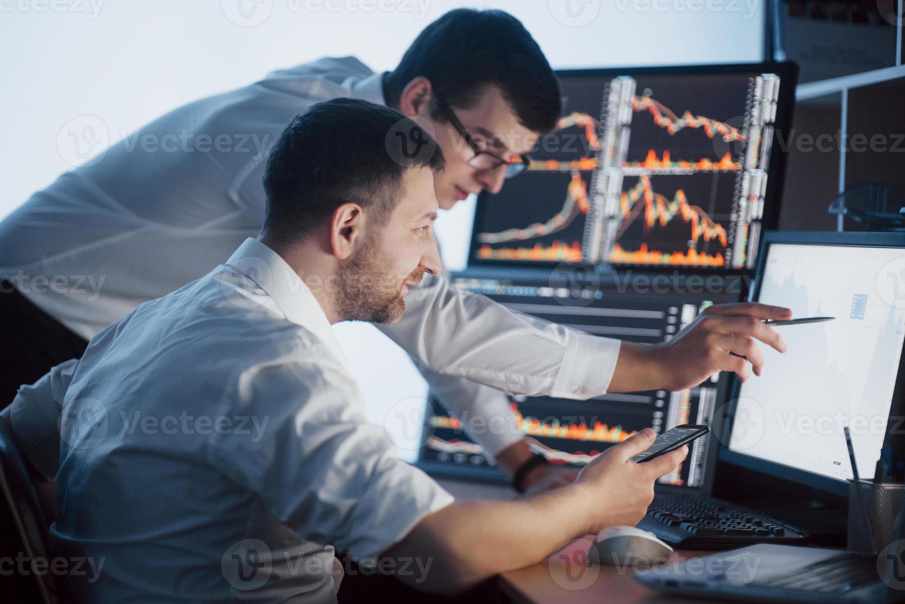 Ein Team von Börsenmaklern unterhält sich in einem dunklen Büro mit Bildschirmen. Analyse von Daten, Grafiken und Berichten für Anlagezwecke. Kreative Teamwork-Händler foto