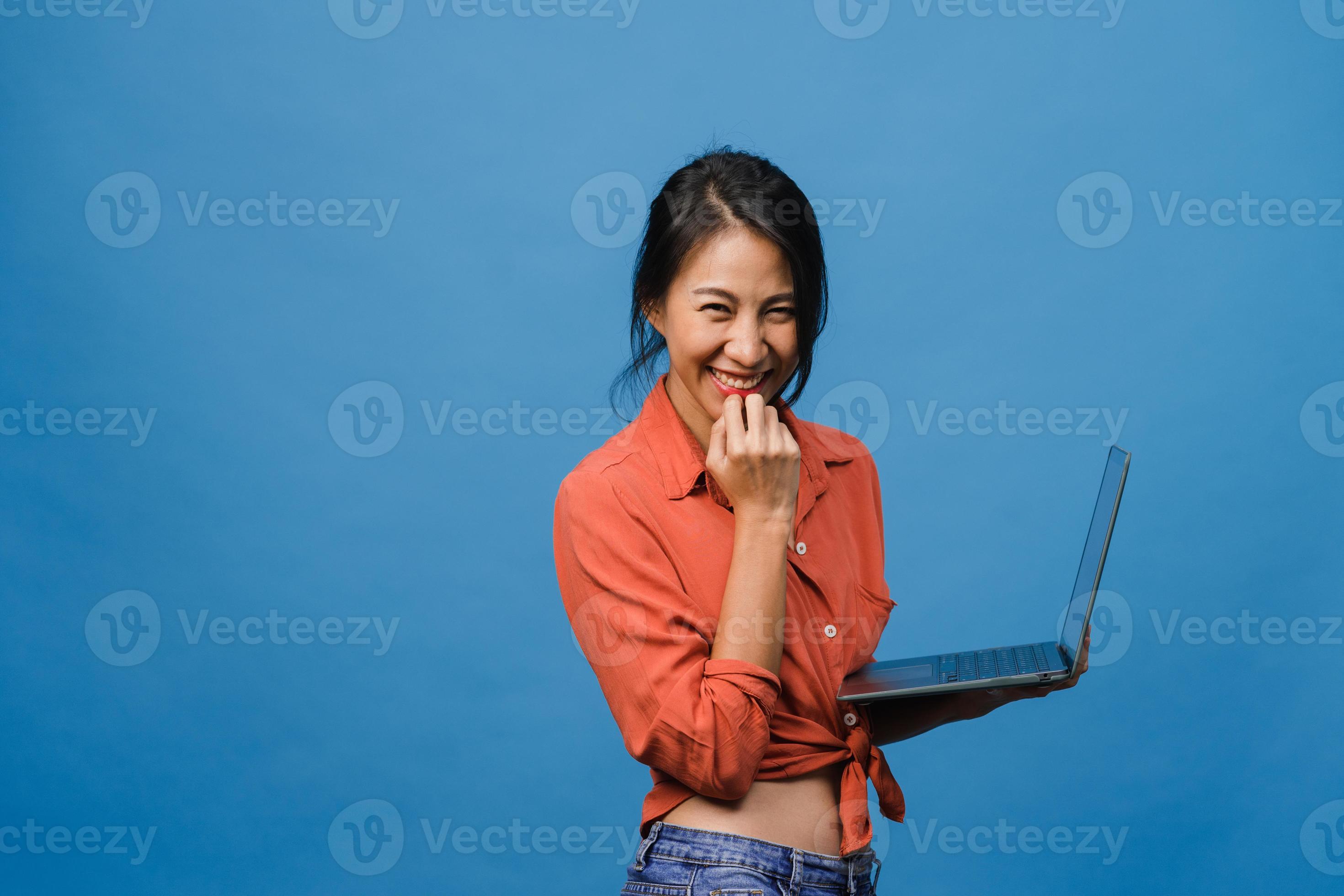 Überraschte junge Asiatin mit Laptop mit positivem Ausdruck, breites Lächeln, in Freizeitkleidung gekleidet und mit Blick auf die Kamera auf blauem Hintergrund. glückliche entzückende frohe frau freut sich über erfolg. foto