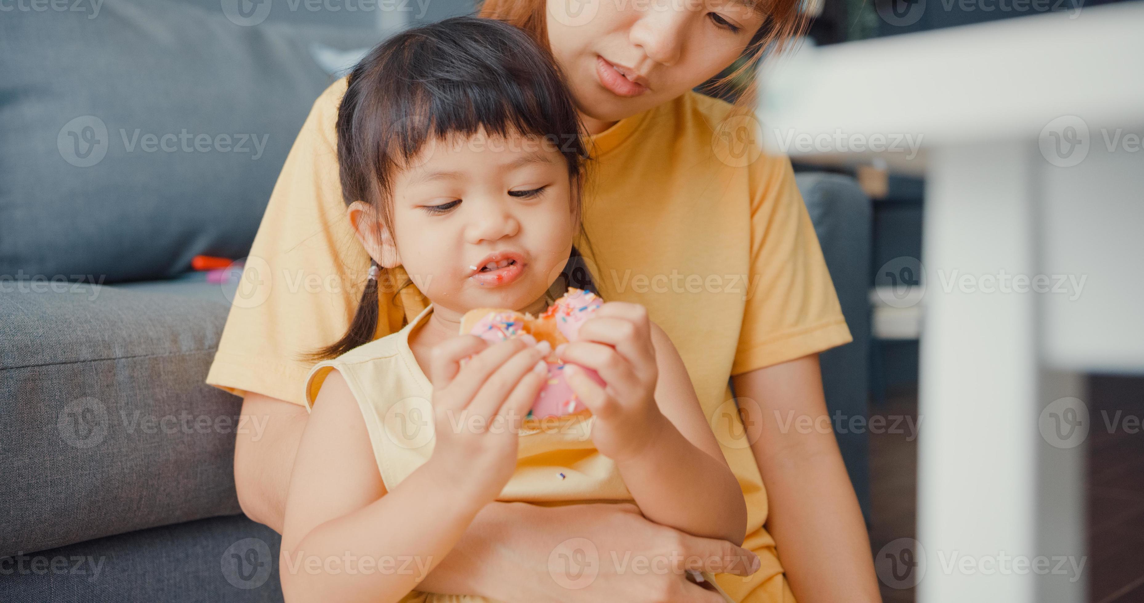 Fröhliche, fröhliche Asien-Familienmutter und Kleinkindmädchen, die Donuts essen und Spaß haben, entspannen Sie sich auf der Couch im Wohnzimmer im Haus. Zeit miteinander verbringen, soziale Distanz, Quarantäne für Coronavirus. foto