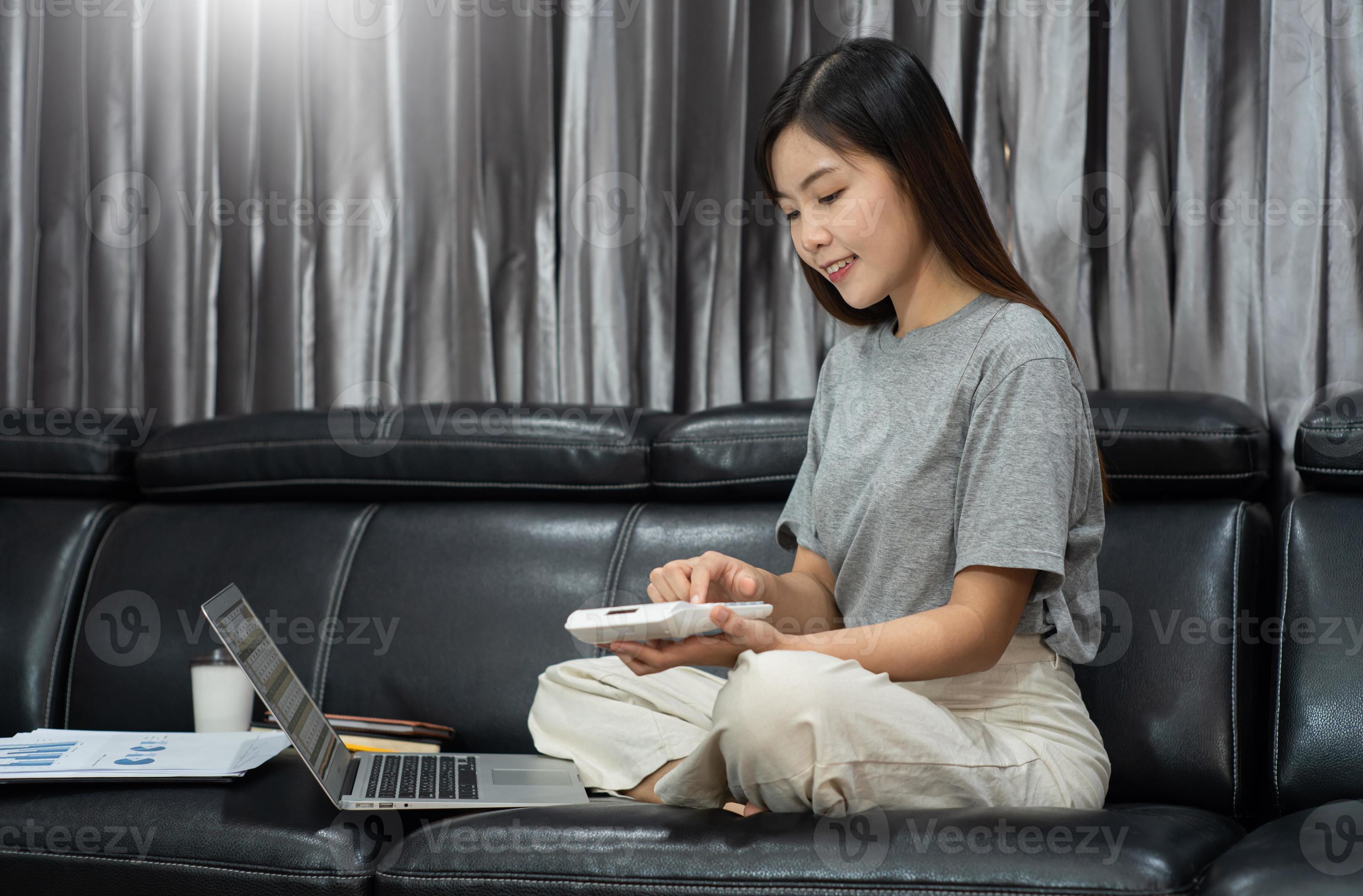 Attraktive junge schöne asiatische Frau, die mit Laptop und Dokument arbeitet, während sie als Freiberuflerin im Wohnzimmerbüro im Innenbereich sitzt, E-Coaching-Arbeit, Fernarbeit oder Arbeit von zu Hause aus. foto