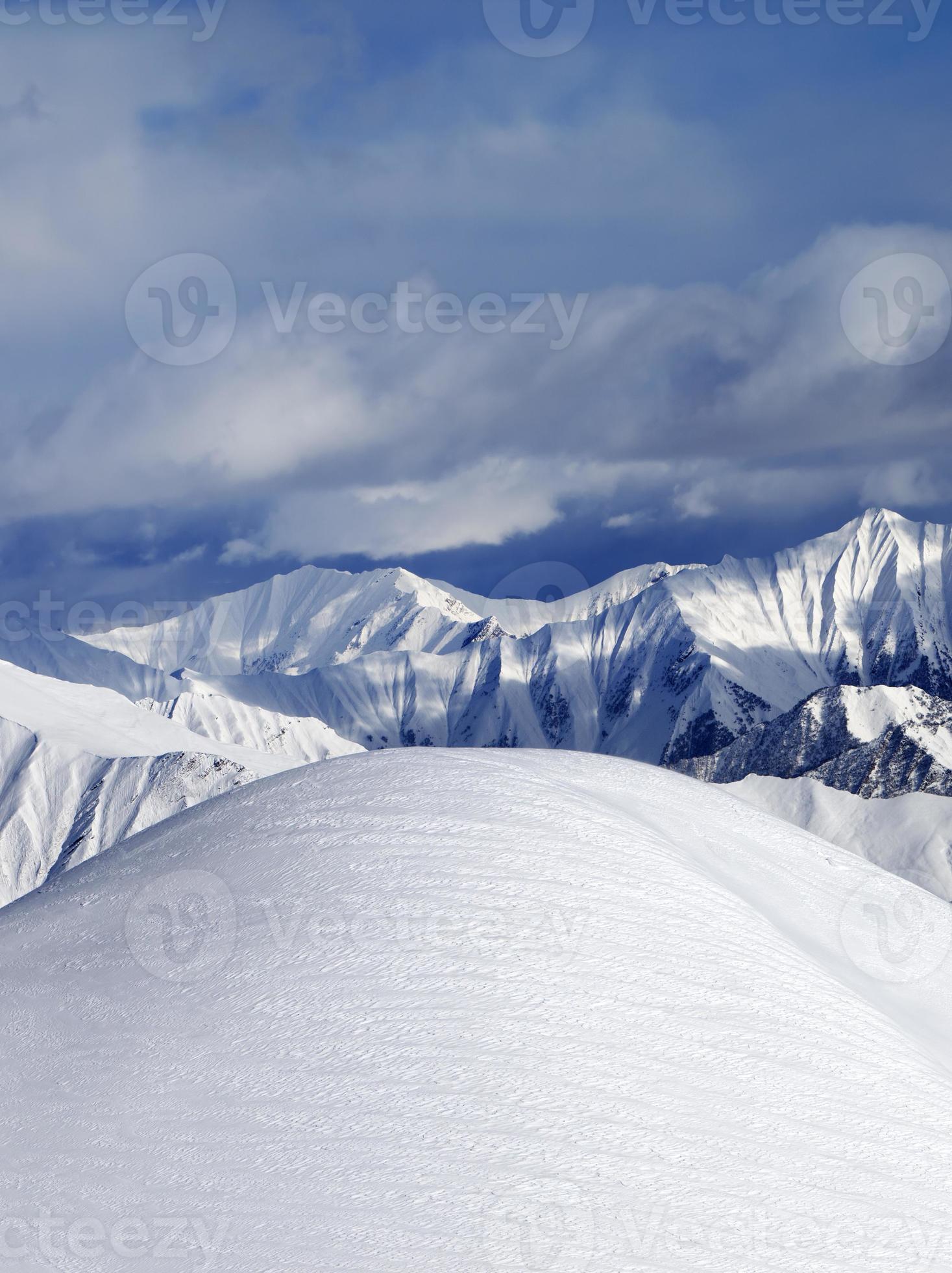 Spitze eines schneebedeckten Abhangs abseits der Piste und bewölkter Berge foto