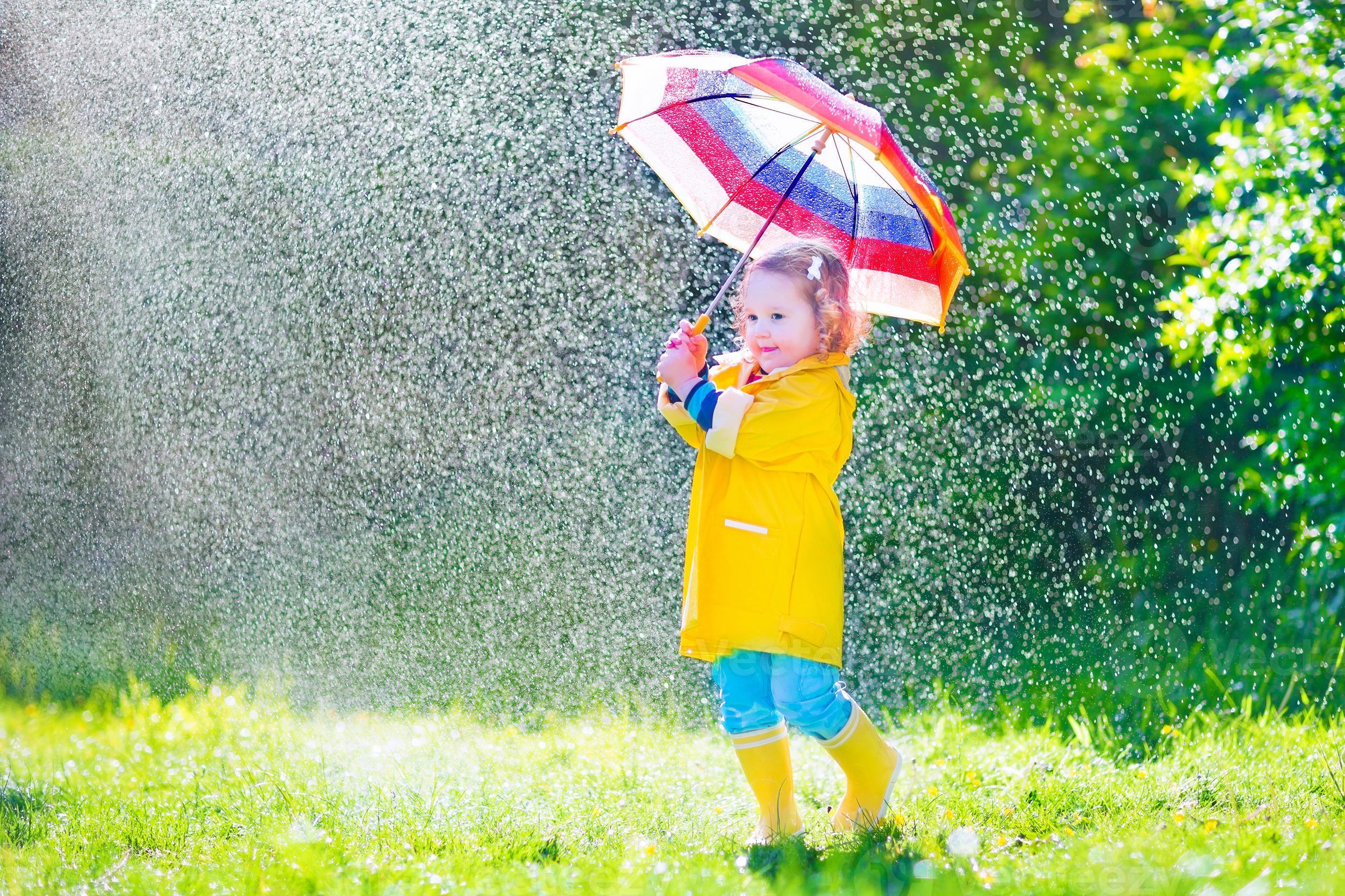lustiges Kleinkind mit Regenschirm, der im Regen spielt foto