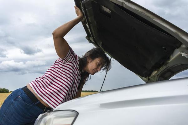 ein kaputtes Auto. eine junge frau steht mitten im nirgendwo neben