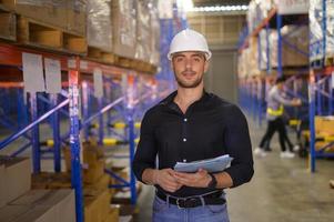 junger arbeiter mit helm, der bestand überprüft und produkt im regal in einem modernen lager zählt. foto