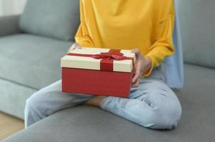 junge überraschte muslimische frau, die eine geschenkbox im wohnzimmer öffnet. foto