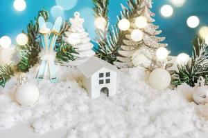 abstrakter Adventsweihnachtshintergrund. Spielzeugmodellhaus und Winterdekorationsverzierungen auf blauem Hintergrund mit Schnee. weihnachten mit familienkonzept zu hause. foto
