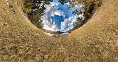 Transformation eines kleinen Planeten mit Raumkrümmung. sphärisches 360-Grad-Panorama am Ufer des Sees im sonnigen Sommer mit fantastischen Wolken. foto