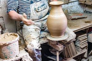 Handwerker in schmutziger Kleidung, der Ton auf der Töpferscheibe in die gewünschte Form bringt. foto